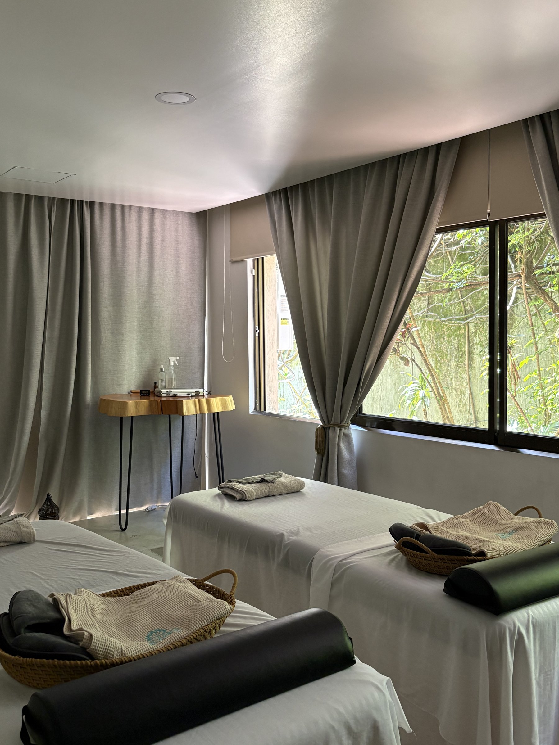 Sala de camillas del spa, cortinas abiertas hacia los árboles de afuera